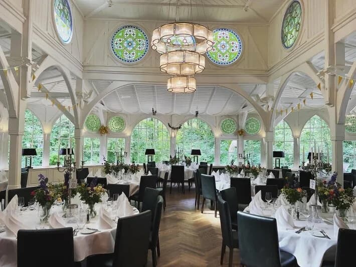 Jugendstil-Saal im LewensLust bei Hildesheim mit weißen Ziersäulen, Rundbogenfenstern und festlich gedeckten runden Tischen